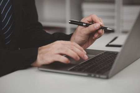 Person typing on laptop keyboard, businessman working on laptop, he is typing messages to colleagues and making financial information sheet to sum up the meeting.の写真素材