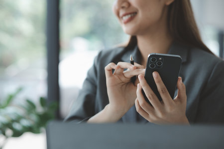 Woman holding a mobile phone and surfing the internet, executing apps on smartphone, answering emails and texting with colleagues. The concept of using technology in communication.の写真素材