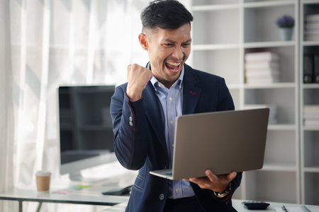 Man holding laptop and celebrating, he is young energetic businessman, modern business management, start-up company run by young people, modern entrepreneur with fresh ideas. to be a business leader.の写真素材
