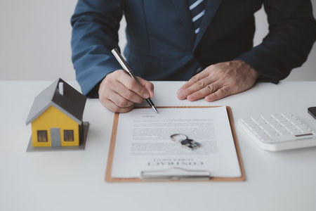 House and real estate agents, house salesmen with house models and house purchase contract documents of housing projects, providing detailed information about real estate. Real estate trading concept.の写真素材