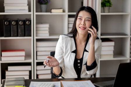 Beautiful asian woman talking on the phone, businesswoman working in office attentively to grow and modernize start-up business, she is analyzing company's market and financial data.の写真素材