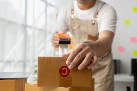 Male owner of an online store packs products into parcel boxes based on orders from online sales sites, packs products for delivery to addresses via private courier service. Product packaging concept.の写真素材