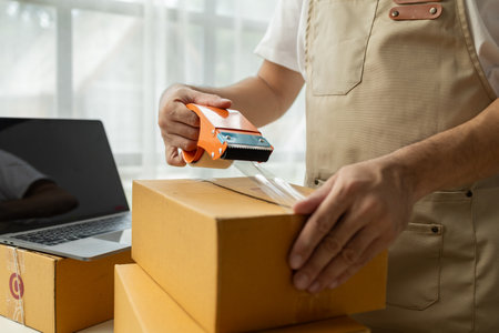 Male owner of an online store packs products into parcel boxes based on orders from online sales sites, packs products for delivery to addresses via private courier service. Product packaging concept.の写真素材
