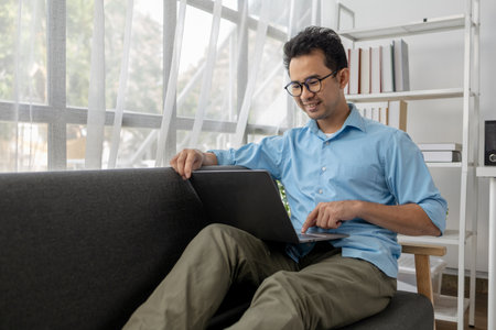 Asian man relaxing in the living room of his home, he is spending the weekend to relax, spending his...