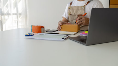 Person writing a customer's address on a parcel box, selling products online, packing orders from customers who order through online shopping sites. Concept of selling products online and e-commerce.の写真素材