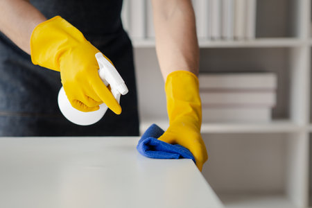 Person cleaning the room, cleaning staff is using cloth and spraying disinfectant to wipe the tables in the company office room. Cleaning staff. Maintaining cleanliness in the organization.の写真素材