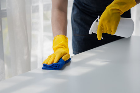 Person cleaning the room, cleaning staff is using cloth and spraying disinfectant to wipe the desk in the company office room. Cleaning staff. Maintaining cleanliness in the organization.の写真素材