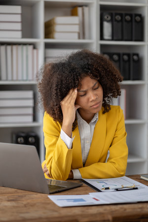 American woman sitting in a startup company, American businesswoman working in the office, she is stressfully looking through financial documents and sales data to summarize before attending a meetingの写真素材