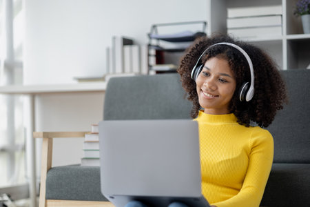 American woman sits in living room on weekends, she is wearing headphones listening to music and spending her days off social media watching movies and listening to music. Holiday activities concept.の写真素材