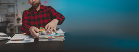 Office worker with stacks of documents, he is a startup company employee working in the office, working overtime, organizing office documents. Concept of working on important documents.の写真素材