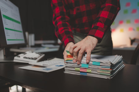 Office worker with stacks of documents, he is a startup company employee working in the office, working overtime, organizing office documents. Concept of working on important documents.の写真素材