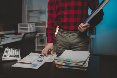 Office worker with stacks of documents, he is a startup company employee working in the office, working overtime, organizing office documents. Concept of working on important documents.の写真素材