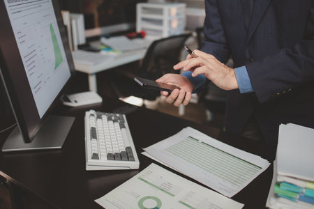 Asian male businessman working in the room. Startup company employee is pressing smartphone to view information, he is in office at night, working overtime, lots of work, hard work. Overtime concept.の写真素材