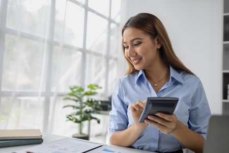 Asian woman working in startup company office, businesswoman checking documents and company performance report to analyze and find ways to grow company. Business administration concept.の写真素材