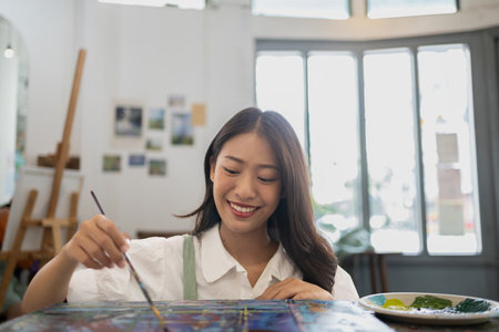 Asian woman is painting art. She is a professional artist. Watercolor artist is painting art on paper. Freelance artist paints with watercolor. Creative art work with watercolor. Art drawing ideas.の写真素材