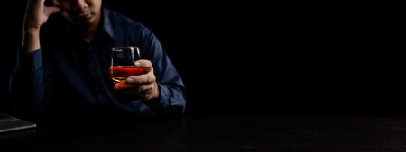 A man drinks whiskey, a businessman relieves stress from work sitting and drinking whiskey in the office after finishing a hard job, a drunk man. Alcohol drinking concept.の写真素材
