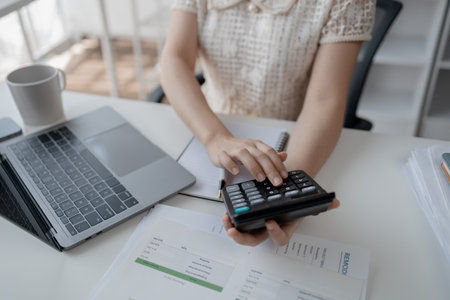 Young Asian business woman in finance presses calculator, business woman works in finance, financial planning for startup company and checking financial statements. Financial management concepts.の写真素材