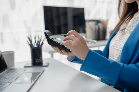 Young Asian business woman in finance presses calculator, business woman works in finance, financial planning for startup company and checking financial statements. Financial management concepts.の写真素材