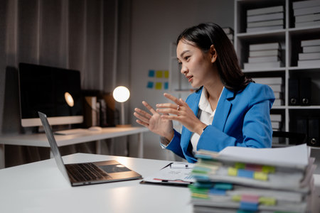 Asian woman is in office of a startup company, young businesswoman is giving a presentation via online video call to group of company executives, presenting a management budget. Online meeting ideas.の写真素材
