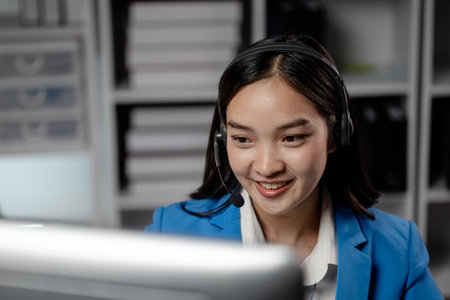 Asian woman wearing headphones and talking to customers. Call center employees answer the phone to help and answer questions from customers who call to use the service. Call center concept.の写真素材