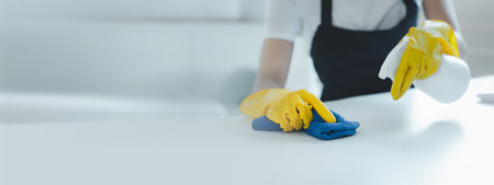 Cleaning desk surface in office with sanitizer spray, wear gloves and wipe the table with a towel,...