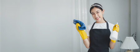 Asian women wear uniforms to prepare for housekeeping work, Wear an apron and rubber gloves to protect against cleaning chemicals, housekeeper is smiling happily before starting work, cleaning idea.の写真素材
