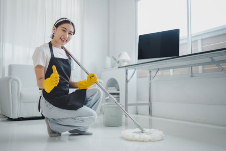 The cleaning staff is checking the floor to see if it is clean or not, Wear rubber gloves and an apron and work with a happy smile, working with cleaning chemicals, cleaning idea.の写真素材