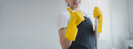 Asian women wear uniforms to prepare for housekeeping work, Wear an apron and rubber gloves to protect against cleaning chemicals, housekeeper is smiling happily before starting work, cleaning idea.の写真素材