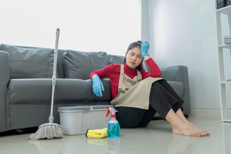 Sit and rest while doing housework, Feeling tired while mopping the floor, Wear an apron and rubber gloves to protect against cleaning chemicals, cleaning idea.の写真素材