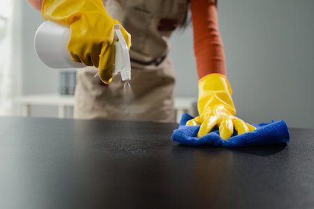 Cleaning desk surface in office with sanitizer spray, wear gloves and wipe the table with a towel.