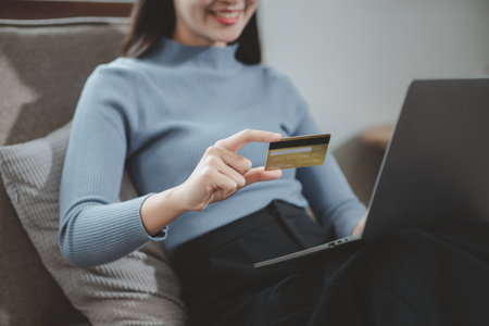 doing online shopping on the sofa in the living room, Use a credit card to make online payments while at home on day off, Use a laptop to enter a credit card information to pay for the service.の写真素材