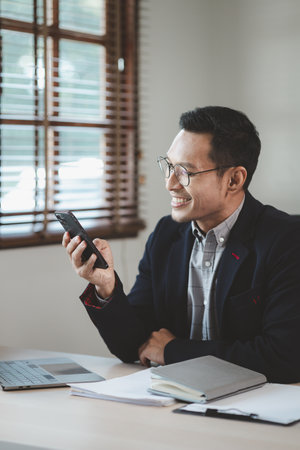Businessman is working in the office and talking on the phone with a partner, Entrepreneurs use smartphones to find information in order to present it, Working in a private office at a company.の写真素材