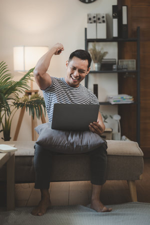 a guy sits and chats with a friend via video call on a couch at home, man using laptop to relax in living room, relaxing idea, Sitting on the sofa at the apartment.の写真素材