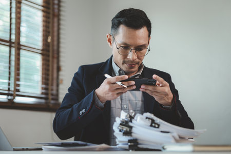 Businessman is working in the office and talking on the phone with a partner, Entrepreneurs use smartphones to find information in order to present it, Working in a private office at a company.の写真素材