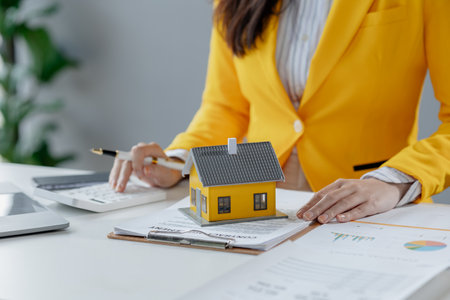 A real estate agent sits in her office, The salesperson is presenting what the home the customer is about to buy looks like, The broker is calculating the buyer's monthly instalment payments.の写真素材