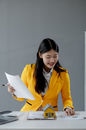 A real estate agent sits in her office, The salesperson is presenting what the home the customer is about to buy looks like, The broker is calculating the buyer's monthly instalment payments.の写真素材