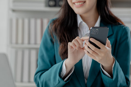 Businesswoman is working in the office and talking on the phone with a partner, Entrepreneurs use smartphones to find information in order to present it, Working in a private office at a company.の写真素材