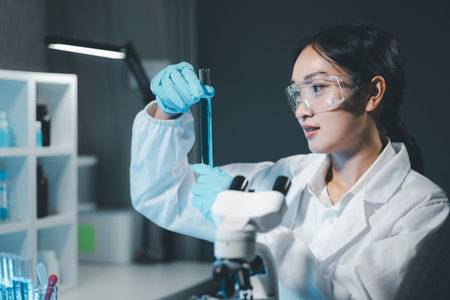 Young scientists in sterile clothing and safety goggles sitting at table conducting research investigations in a medical laboratory using a microscope, Serious concentrated female microbiologist.の写真素材