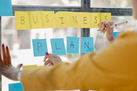 Collaboration is a key to best results. young modern people in smart casual wear planning business strategy while young woman pointing at infographic displayed on the glass wall in the office.の写真素材
