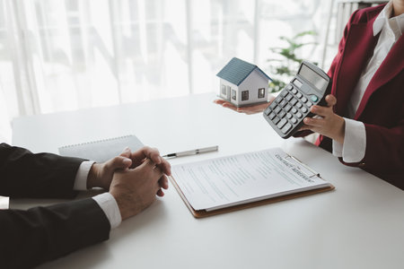 A real estate agent sits in her office, The salesperson is presenting what the home the customer is about to buy looks like, The broker is calculating the buyer's monthly instalment payments.の写真素材