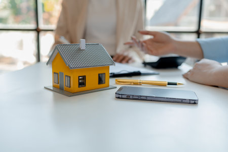 A real estate agent sits in her office, The salesperson is presenting what the home the customer is about to buy looks like, The broker is calculating the buyer's monthly instalment payments.の写真素材