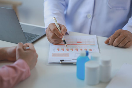 male medical practitioner reassuring a patient, Doctor and patient in conversation, Asian male doctor consulting patient, Professional physician wearing white coat talking to mature womanの写真素材