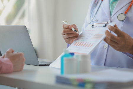 male medical practitioner reassuring a patient, Doctor and patient in conversation, Asian male doctor consulting patient, Professional physician wearing white coat talking to mature womanの写真素材