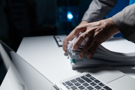 An employee held a large pile of documents in his hand, Large piles of work documents on desks are being sorted by employees, Important documents are stacked.の写真素材