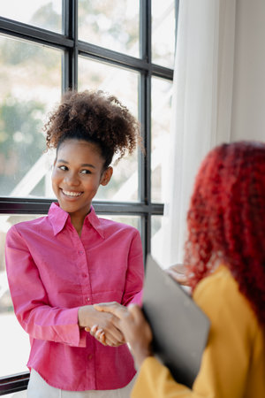 Two beautiful African female were shaking hands in the office as important work has been discussed successfully, beautiful successful African businesswomen are holding hands due to business victory.の写真素材