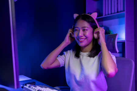 A beautiful female gamer happily plays in a private room with dim lighting that is perfect for creating a gaming mood, She has a passion for playing games, playing games is a hobby.の写真素材