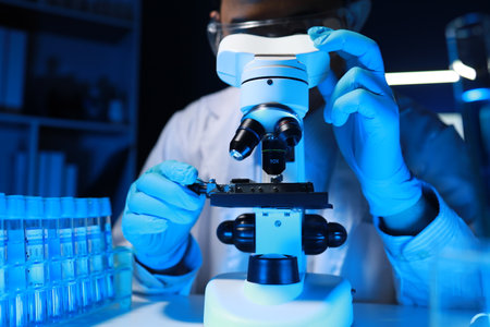 A talented scientist sits in his lab while using a microscope to look for microscopic organisms in a...