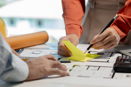 Engineer and architect work together in the office of a construction company, Architect and assistant are reviewing blueprints and writing down their conclusions before meeting with their supervisors.の写真素材
