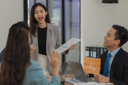 A group of employees happily work together in the office while discussing work that was completed on...