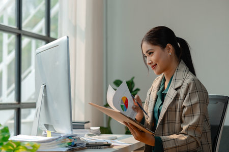 a businesswoman works at her desk, an entrepreneur is sitting and working in front of the computer to research for information on new project, female employee is in the officeの写真素材
